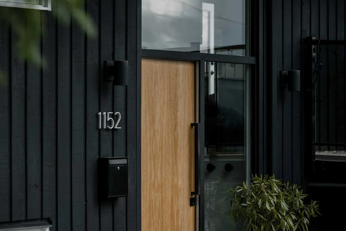New light wood front door set into the black-painted wood exterior