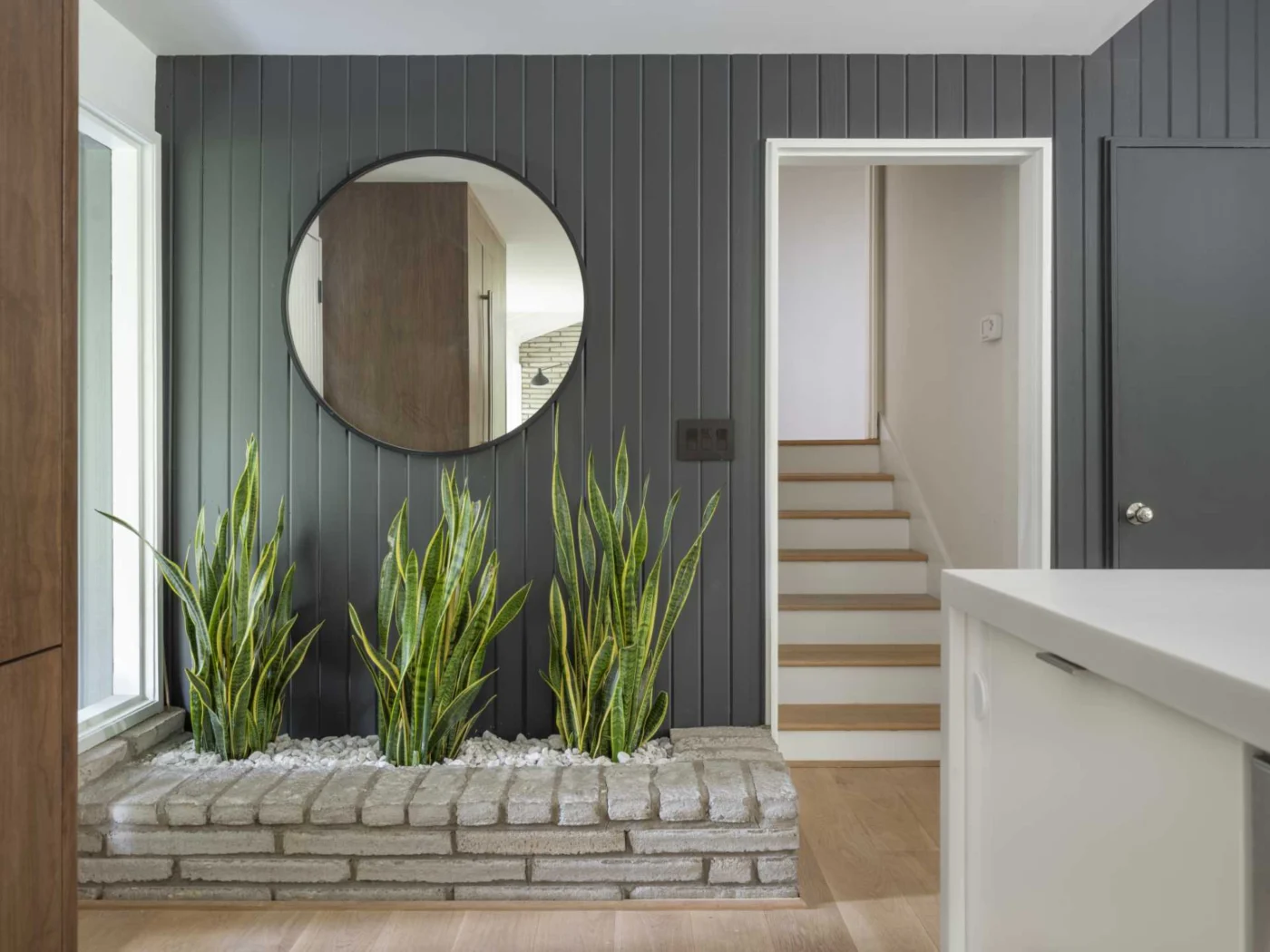 Updated entryway with the original brick planter, grey painted wood and a large round mirror
