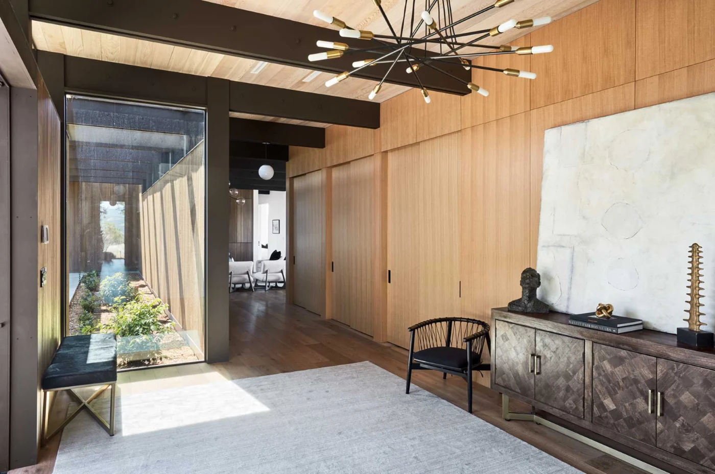 Entryway with a bench, a sculptural chandelier and a wood wall concealing doors