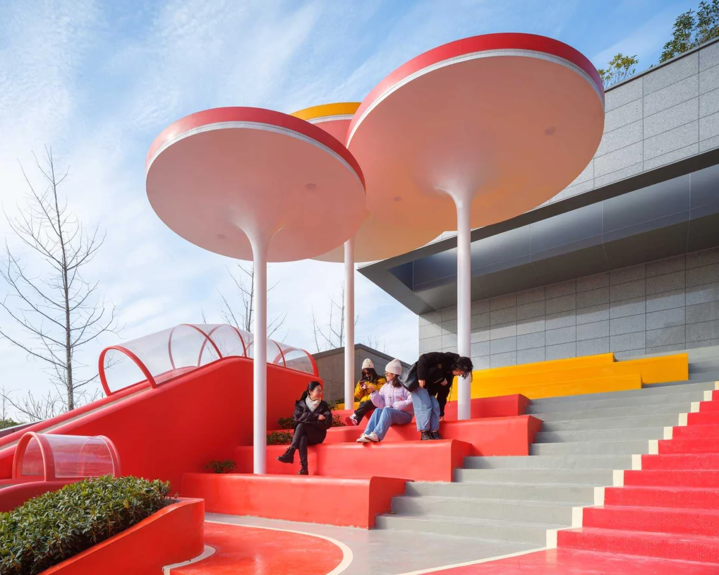 Residents sitting on red steps beneath large disc-shaped shades