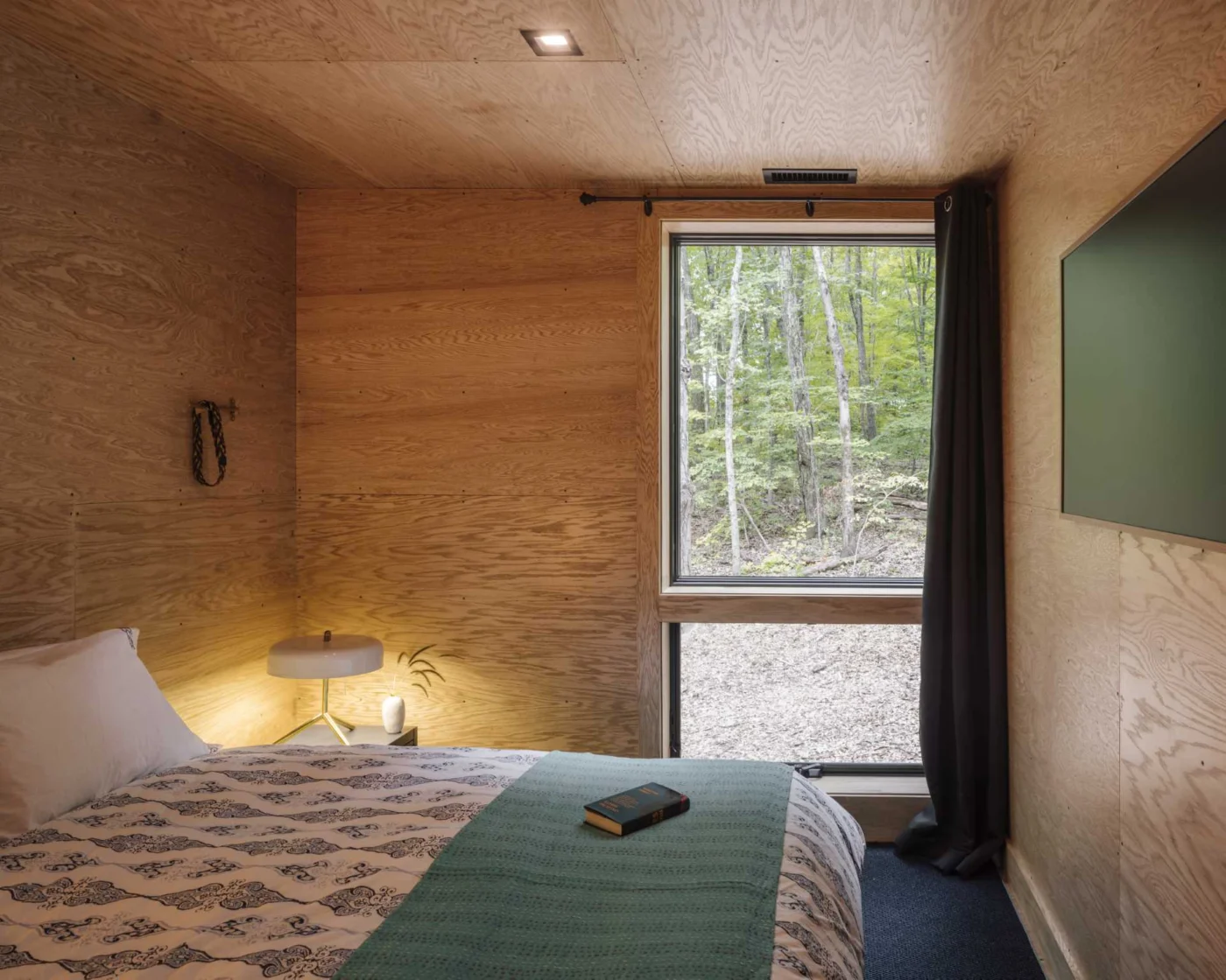Wood-lined bedroom with a vertical window looking into the forest