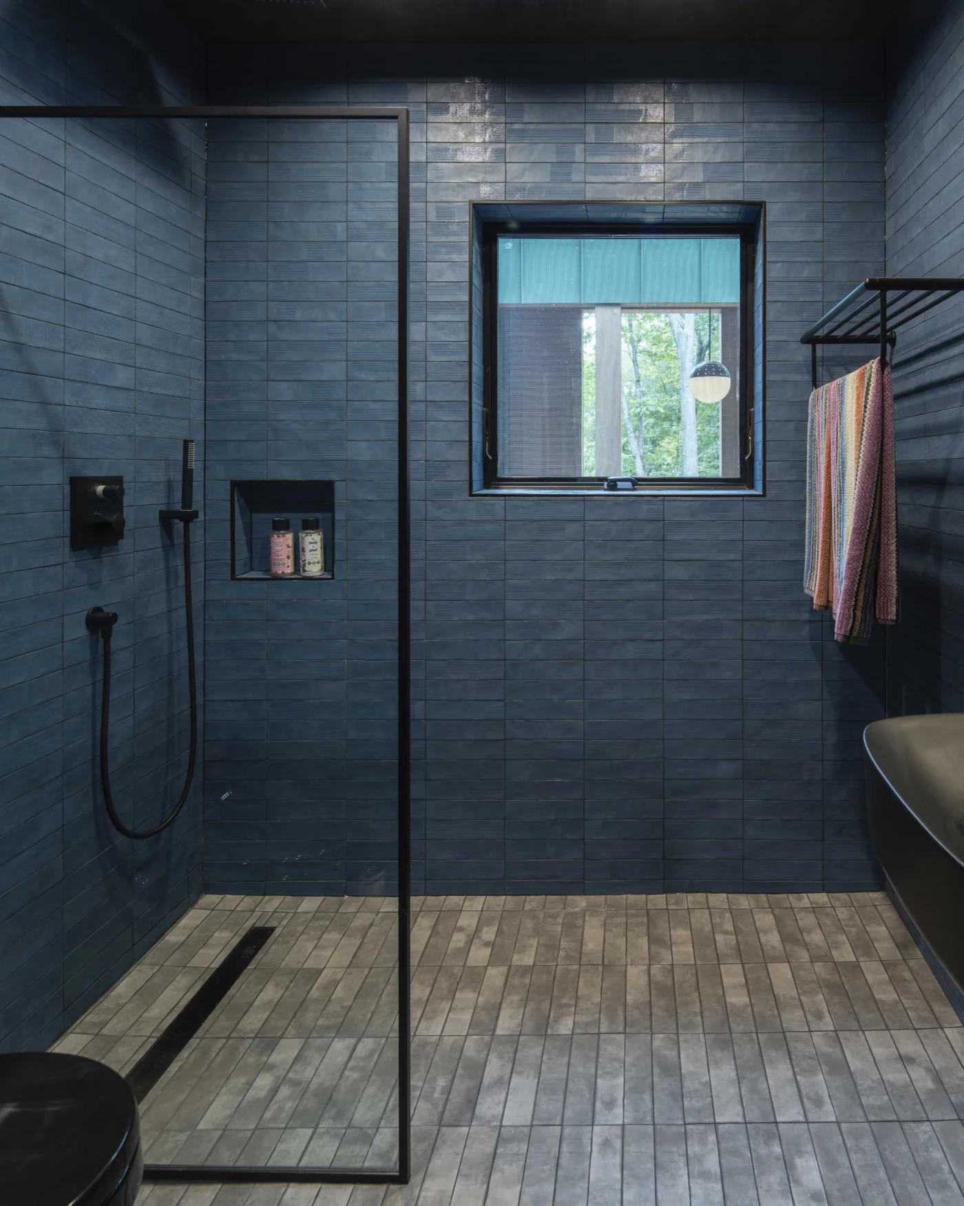 Bathroom with dark blue wall tiles, grey floor tiles and black fittings