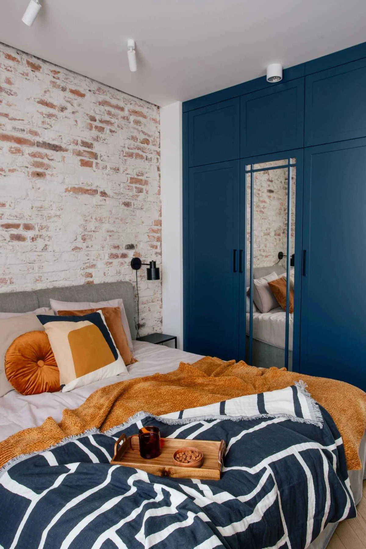 Bedroom with an exposed structural brick wall and deep blue cabinetry around a mirror