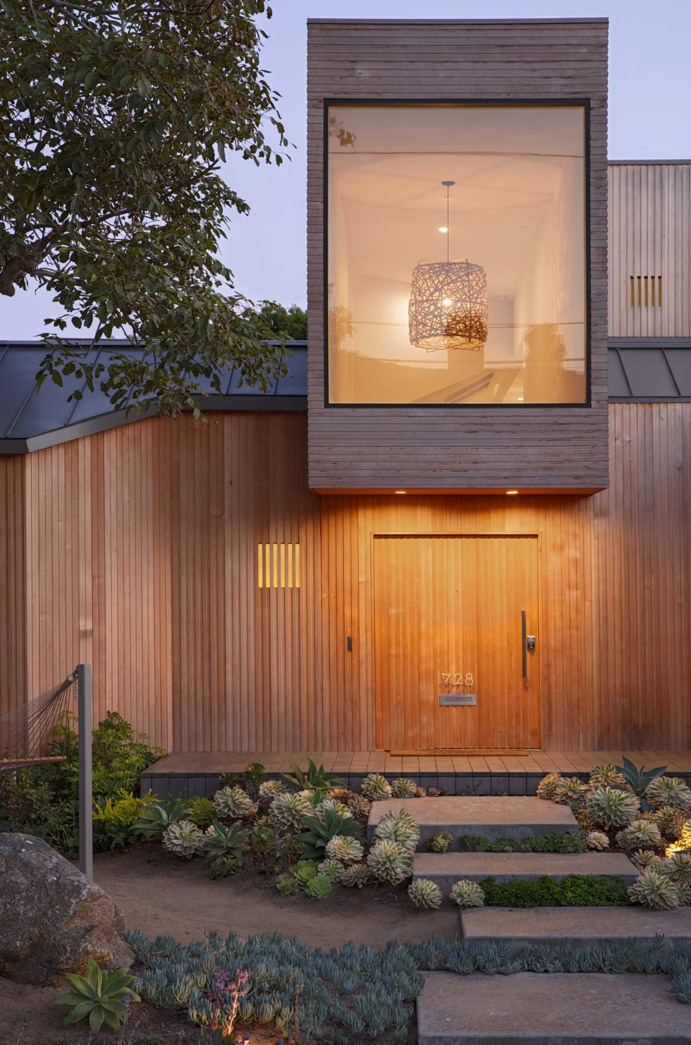 The cedar-clad house glowing with exterior lighting at night