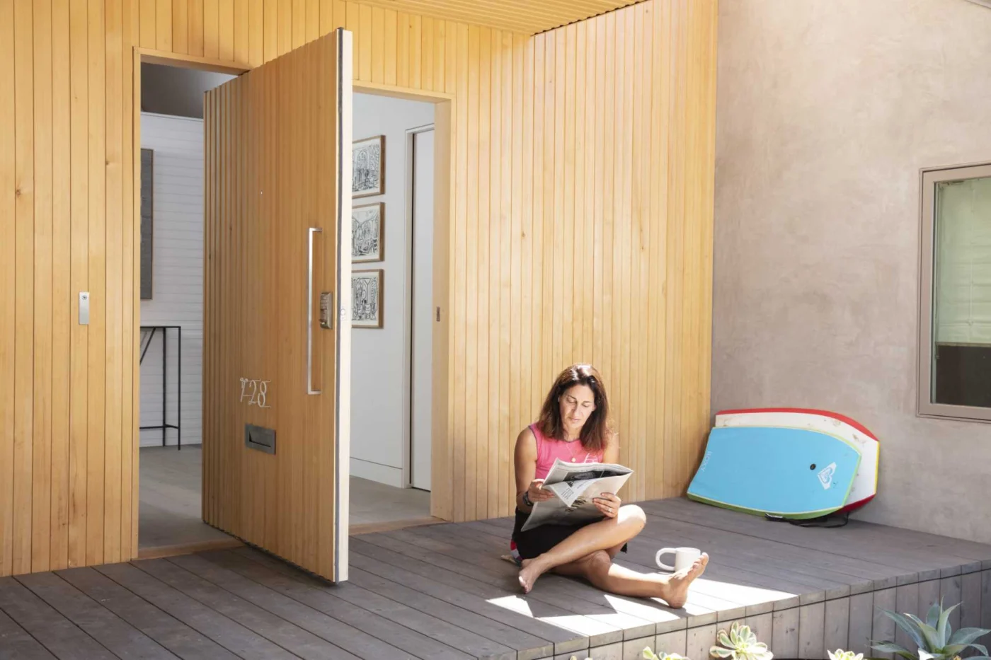 Wood-covered pivot front door opening to a white entryway with artwork and a console