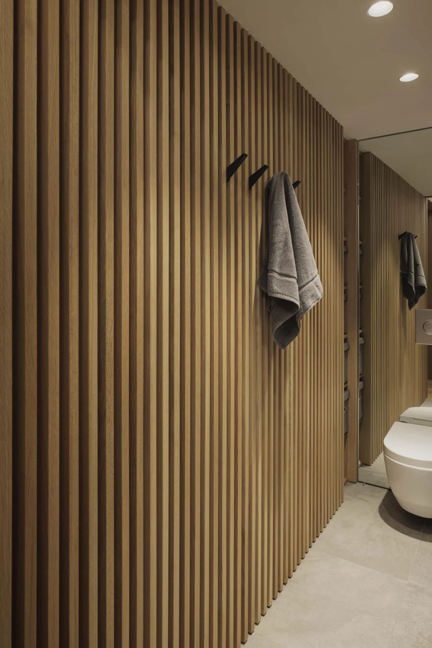 Full-height oak slat wall with black hooks by the bathroom