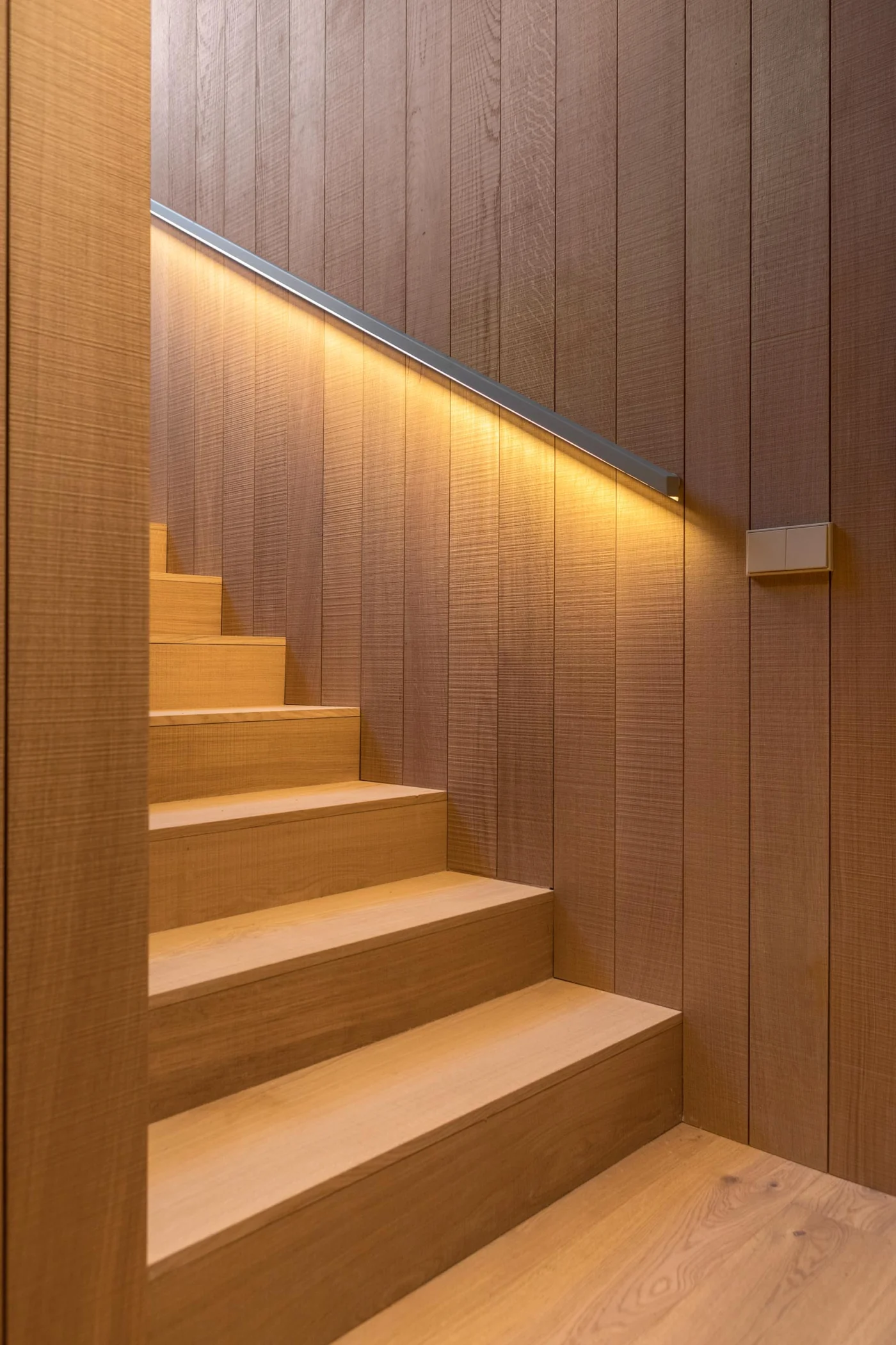Wood stairs with a handrail lit by hidden lighting